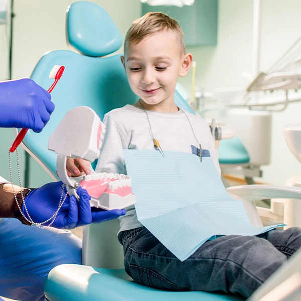 Boy In Dental Chair Looking At Tooth Model